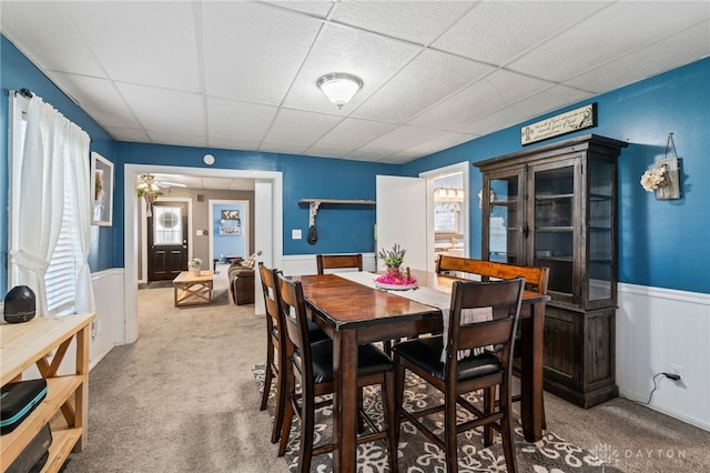 carpeted dining space featuring a paneled ceiling and a wainscoted wall
