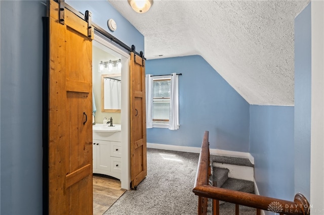 interior space featuring a sink, a textured ceiling, baseboards, a barn door, and lofted ceiling