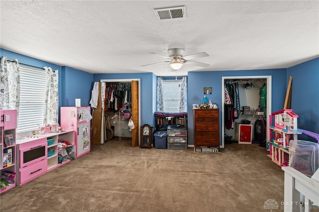 playroom featuring a textured ceiling, carpet flooring, a ceiling fan, and visible vents
