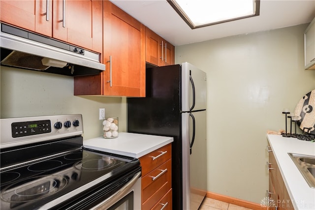 kitchen featuring under cabinet range hood, light tile patterned flooring, brown cabinetry, light countertops, and appliances with stainless steel finishes