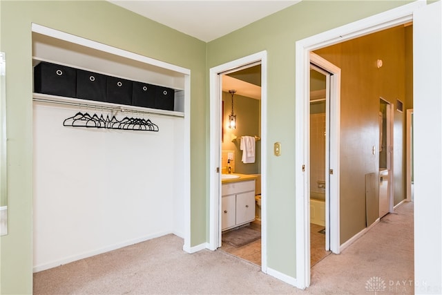 interior space featuring light colored carpet, a sink, and baseboards