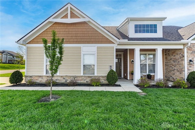 craftsman-style house featuring a porch, roof with shingles, a front yard, and stone siding