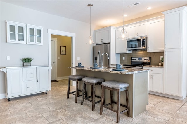 kitchen featuring a kitchen breakfast bar, white cabinetry, decorative backsplash, visible vents, and stainless steel appliances
