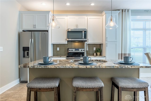 kitchen with decorative backsplash, a kitchen bar, baseboards, white cabinets, and appliances with stainless steel finishes
