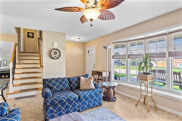 living area with ceiling fan, baseboards, tile patterned flooring, and stairs