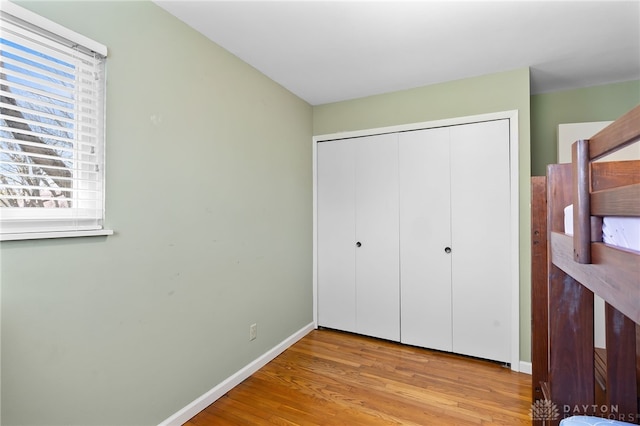 unfurnished bedroom featuring baseboards, wood finished floors, multiple windows, and a closet