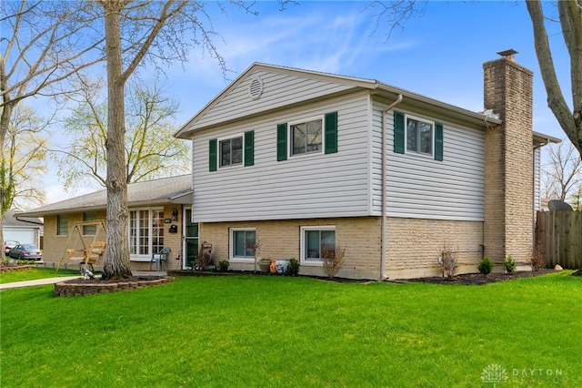 tri-level home with fence, a chimney, brick siding, and a front lawn
