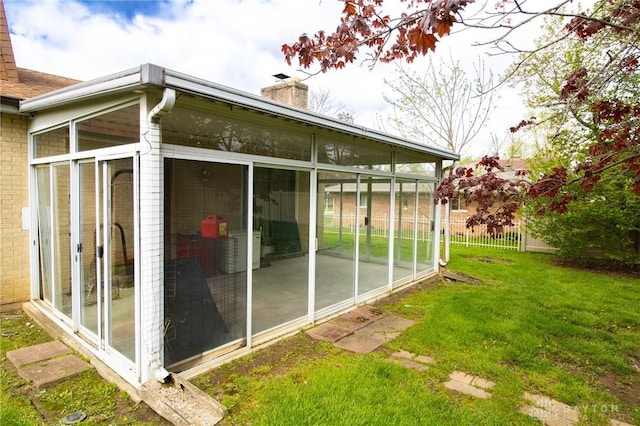 view of property exterior with a chimney, brick siding, fence, and a sunroom