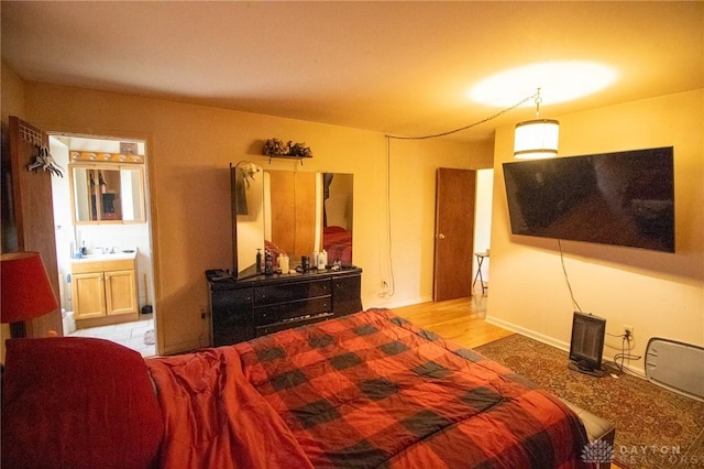 bedroom featuring wood finished floors, ensuite bathroom, and a sink