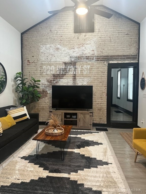 living area with ceiling fan, vaulted ceiling, wood finished floors, and brick wall