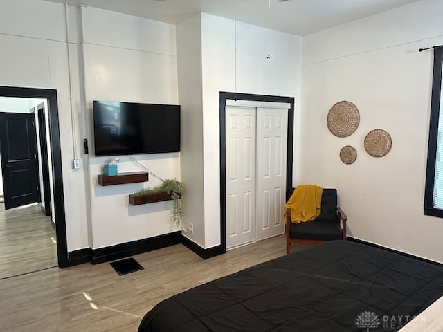 bedroom with baseboards, visible vents, wood finished floors, and a closet
