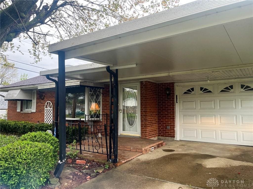 doorway to property featuring driveway, an attached garage, a porch, and brick siding