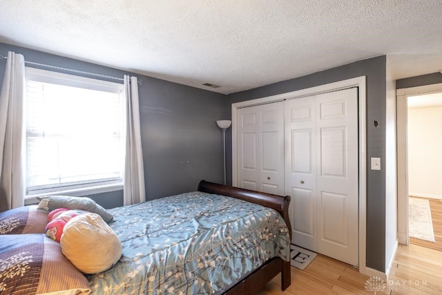 bedroom featuring light wood finished floors, a closet, visible vents, baseboards, and a textured ceiling