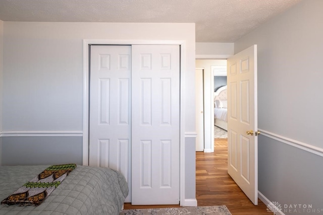 bedroom featuring baseboards, wood finished floors, a textured ceiling, and a closet