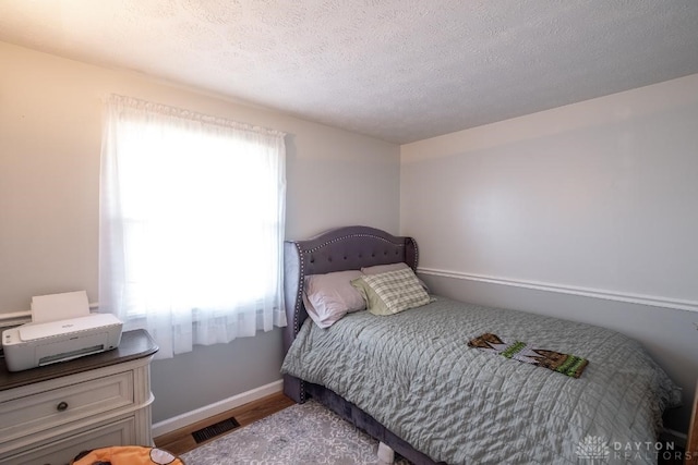 bedroom with baseboards, visible vents, wood finished floors, and a textured ceiling
