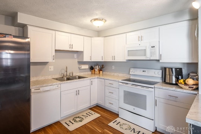 kitchen with wood finished floors, white appliances, light countertops, a sink, and white cabinetry