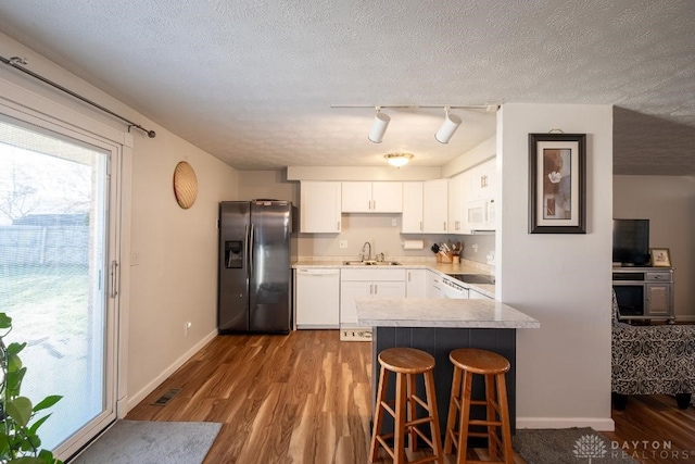 kitchen featuring white cabinetry, a sink, baseboards, dark wood-type flooring, and white appliances
