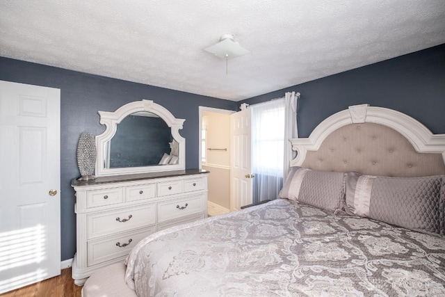bedroom with a textured ceiling, wood finished floors, and baseboards