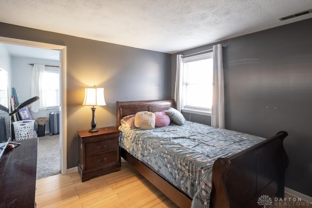 bedroom with a textured ceiling, visible vents, multiple windows, and light wood-type flooring
