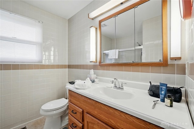bathroom with a shower, vanity, toilet, and tile walls