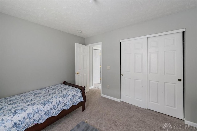 carpeted bedroom featuring a textured ceiling, baseboards, and a closet