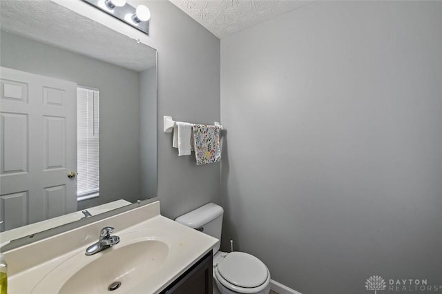 bathroom featuring a textured ceiling, vanity, toilet, and baseboards