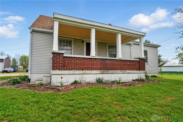 exterior space featuring covered porch, brick siding, a shingled roof, and a front yard