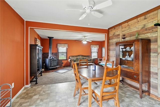dining space with a wood stove, ceiling fan, wood walls, baseboards, and light floors
