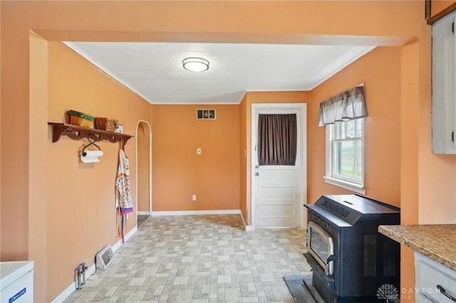 interior space with crown molding, a wood stove, visible vents, baseboards, and laundry area