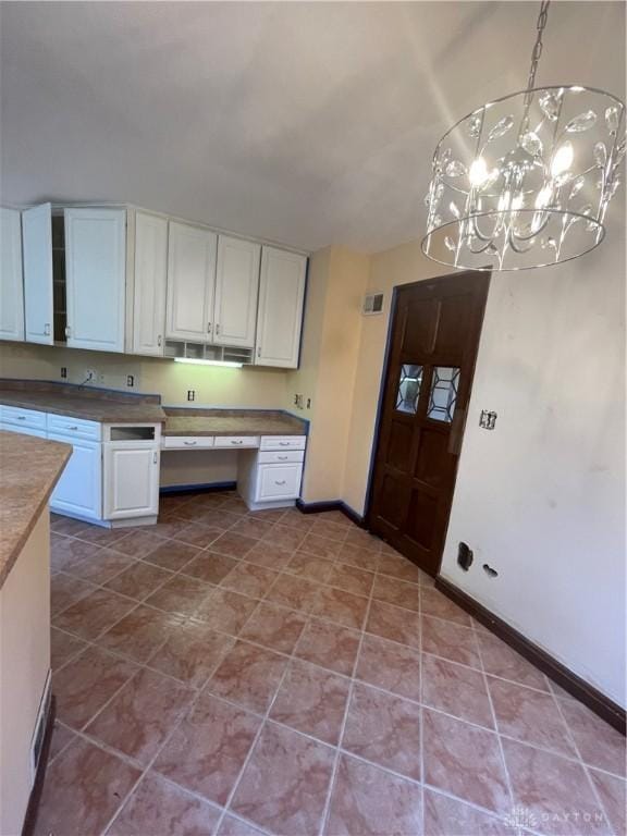 kitchen featuring baseboards, a chandelier, decorative light fixtures, built in desk, and white cabinetry