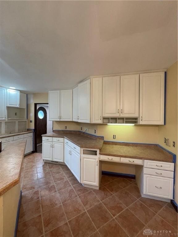 kitchen with dark tile patterned floors, white cabinets, and built in study area