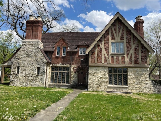 tudor home with a chimney, a front yard, and stone siding