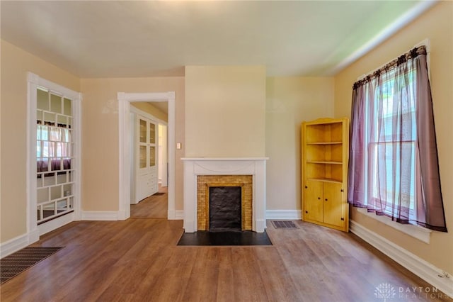 unfurnished living room featuring a fireplace with flush hearth, wood finished floors, visible vents, and a healthy amount of sunlight