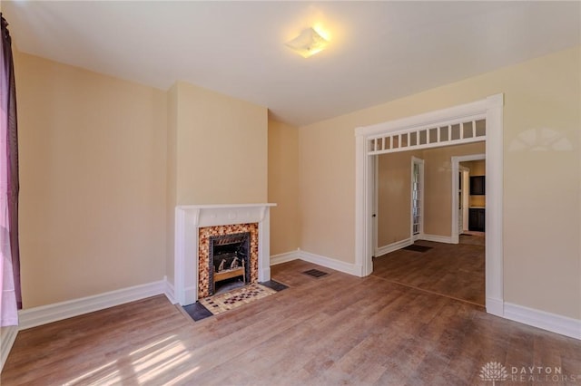 unfurnished living room featuring wood finished floors, visible vents, a premium fireplace, and baseboards