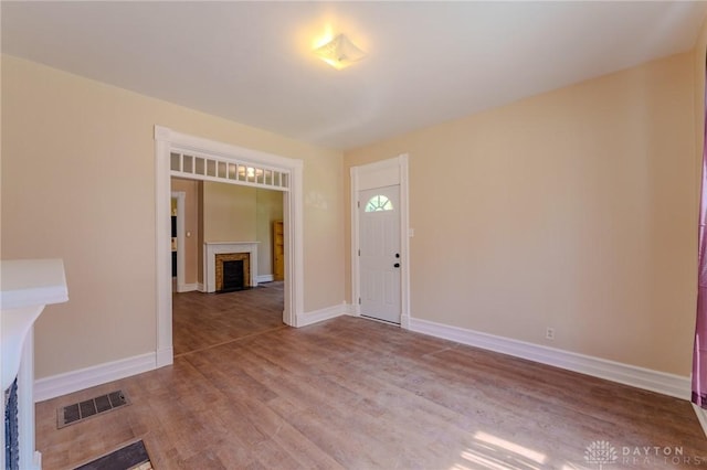 entryway featuring baseboards, visible vents, wood finished floors, and a fireplace with flush hearth