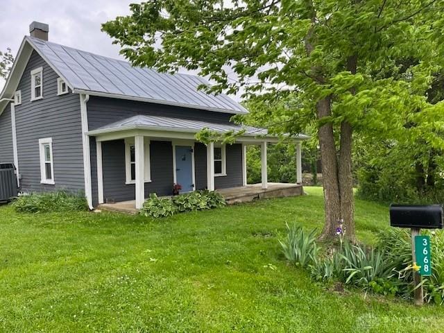 3668 Concord Fairhaven Rd, Eaton, OH 45320 - view of front facade featuring a chimney, covered porch, a front lawn, central AC unit, and metal roof