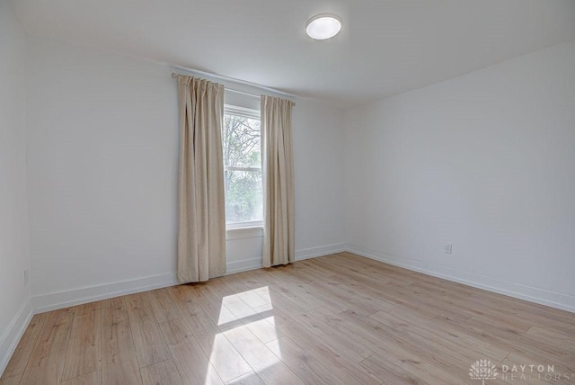 spare room with baseboards and light wood-style floors