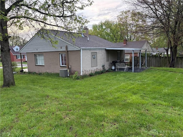 back of house with a chimney, a yard, fence, central AC, and brick siding