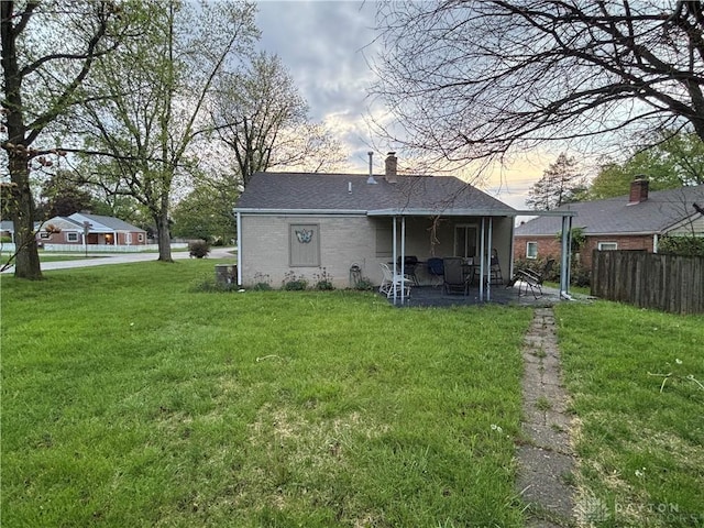 back of property at dusk featuring a patio, fence, a chimney, and a lawn