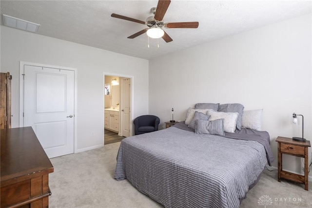 bedroom with a ceiling fan, visible vents, baseboards, light colored carpet, and ensuite bathroom