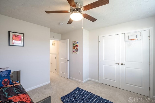 bedroom with a ceiling fan, a closet, light colored carpet, and baseboards