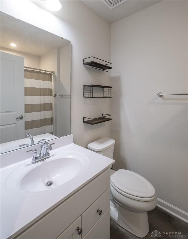 full bathroom featuring wood finished floors, a shower with shower curtain, toilet, vanity, and baseboards