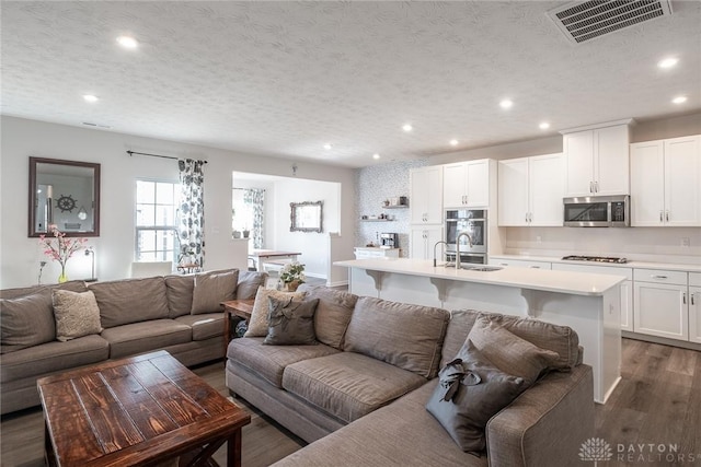 living area with a textured ceiling, visible vents, wood finished floors, and recessed lighting