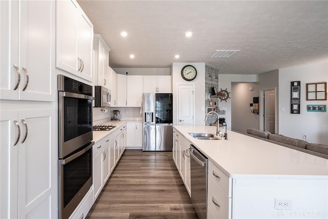 kitchen with a kitchen island with sink, stainless steel appliances, light countertops, dark wood-style flooring, and a sink