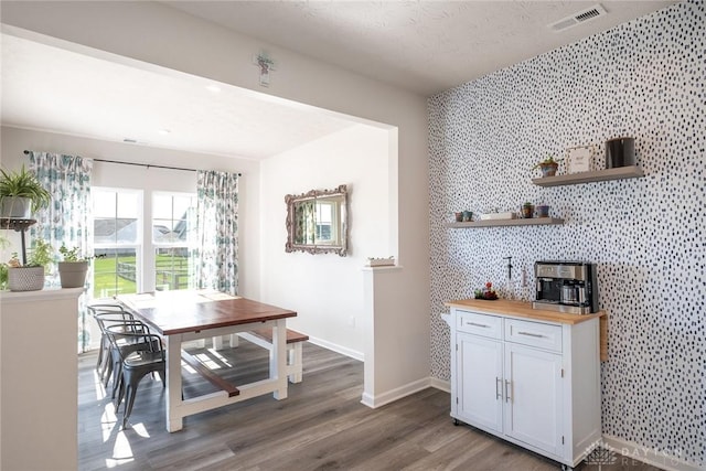 dining area featuring an accent wall, visible vents, wood finished floors, and baseboards
