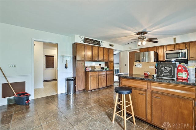 10699 Hamilton Ave, Cincinnati, OH 45231 - kitchen with stainless steel appliances, brown cabinetry, ceiling fan, a kitchen bar, and baseboards