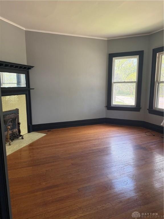 spare room featuring baseboards, wood finished floors, a fireplace with flush hearth, and crown molding