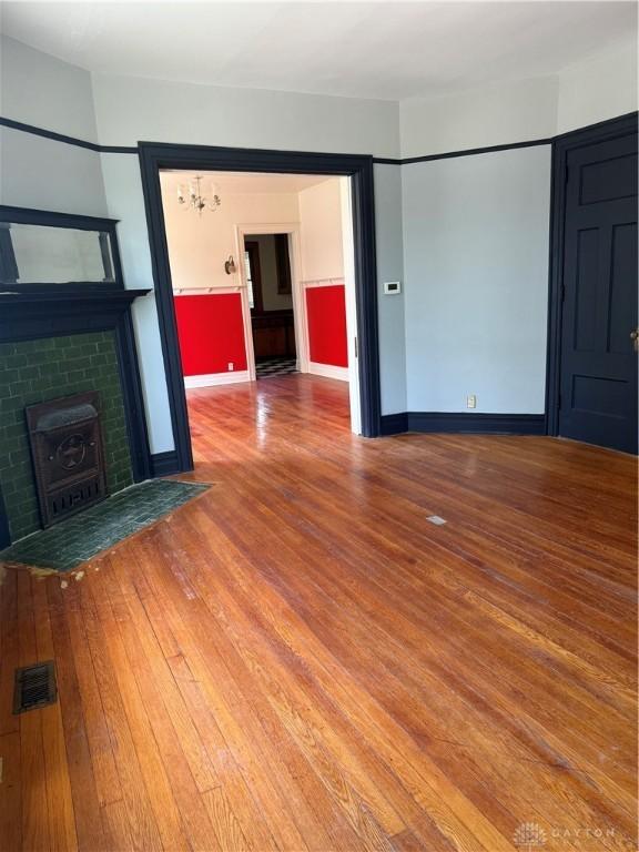 unfurnished living room with a fireplace with flush hearth, hardwood / wood-style floors, baseboards, and visible vents