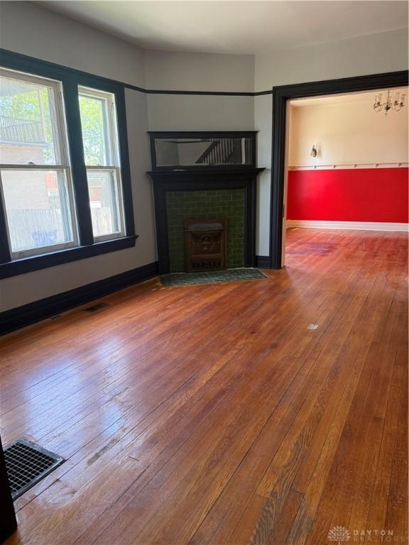 unfurnished living room with visible vents, a tiled fireplace, hardwood / wood-style flooring, and baseboards