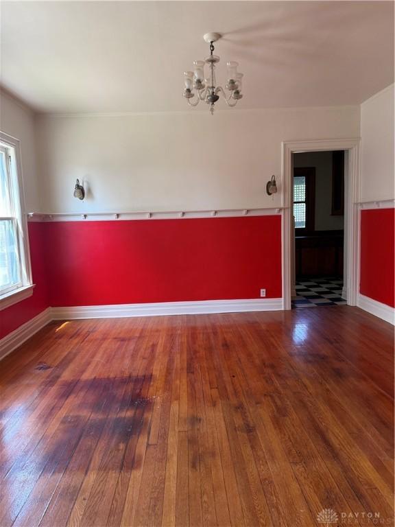 unfurnished room featuring a chandelier, hardwood / wood-style flooring, and baseboards